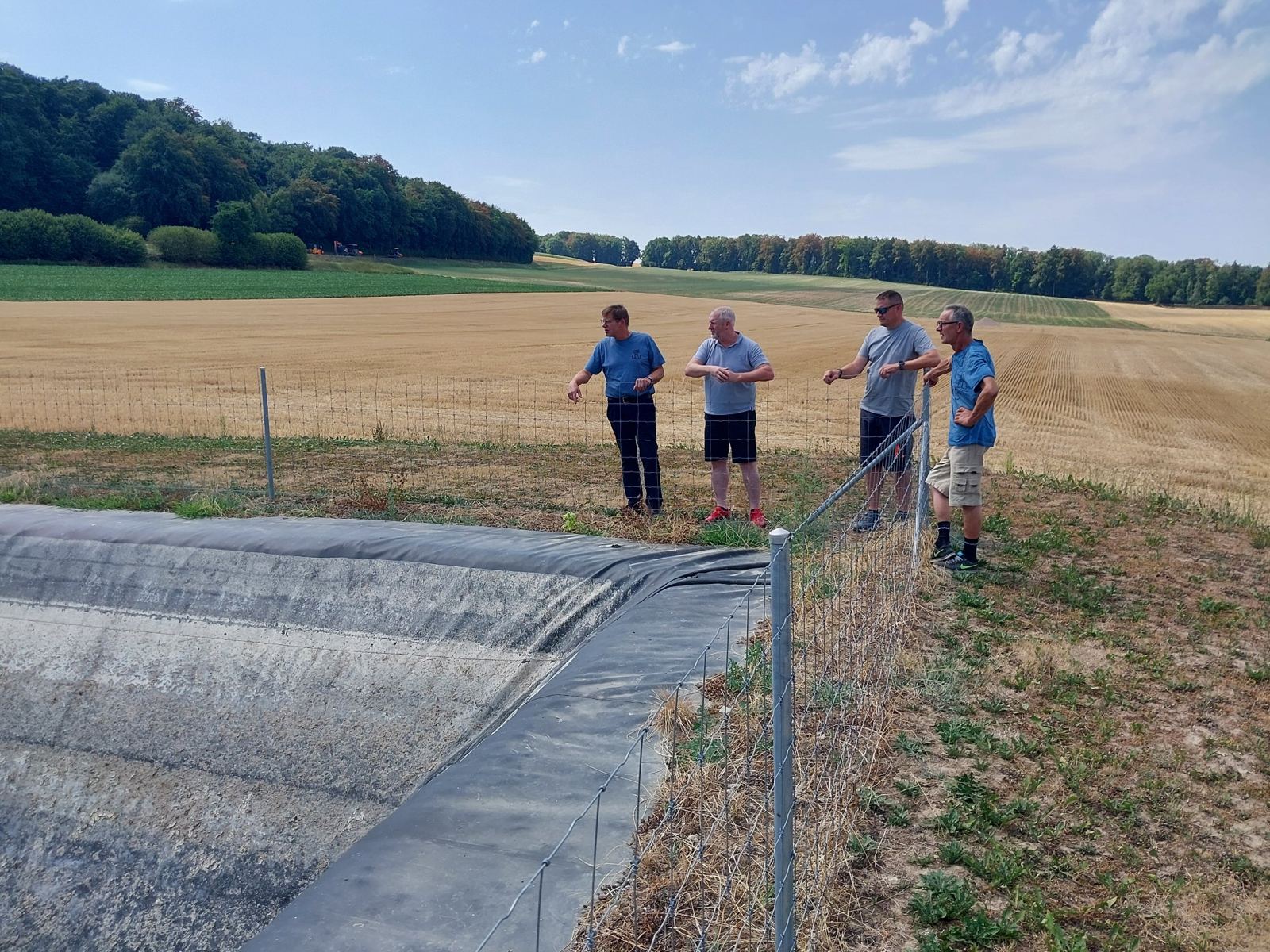 Quatre membres du comité au bord d'un bassin de rétention, devant un champ moissonné